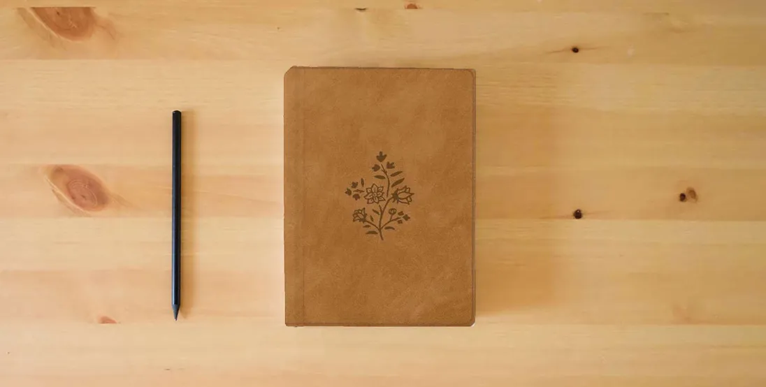 The book ESV Single Column Journaling Bible, Large Print (TruTone, Nubuck Caramel, Wildflower Design)} is on the table