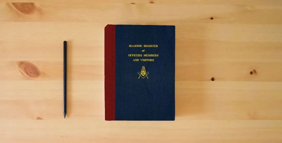 The book Masonic Register of Officers, Members and Visitors} is on the table